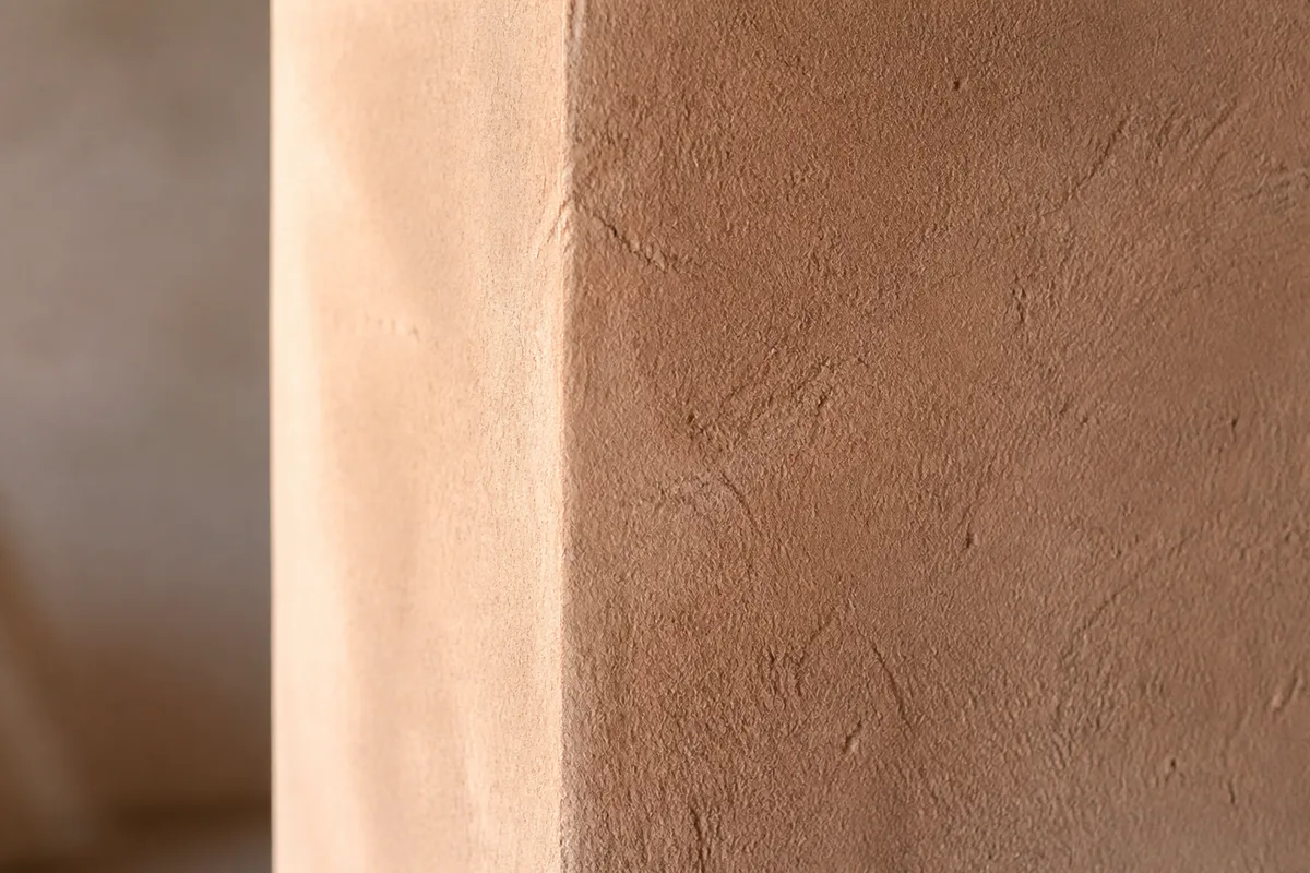 Mur intérieur enduit en terre crue ocre clair sous une lumière rasante