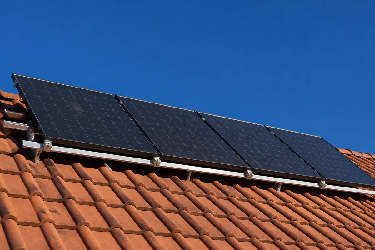 Toiture en tuiles rouges avec rangée de panneaux photovoltaïques posés en surimposition sur rails
